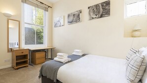 Ein Schlafzimmer mit Bett, Schreibtisch, Stuhl, Fenster und einem Kunstwerk an der Wand.