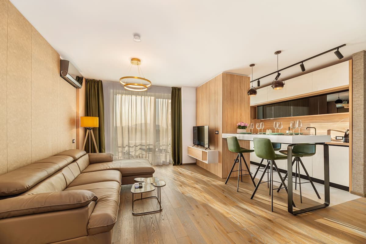 Uma sala de estar moderna com um sofá, uma área de jantar com cadeiras, uma pequena mesa e uma cozinha com bancada e armários.
