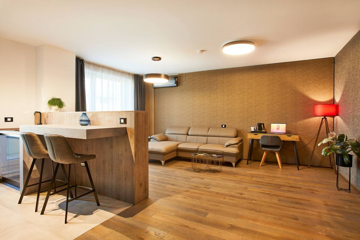 Uma sala de estar moderna com piso de madeira, um sofá, uma escrivaninha com computador e um abajur vermelho.