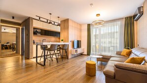 A modern living room with a sofa, a dining area with chairs, a kitchen with a TV, and a large window with curtains. - Promenada Studios (Brasov)