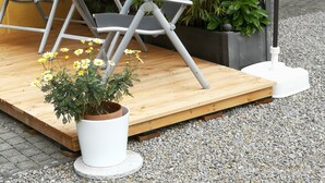 Um pátio com duas cadeiras, uma mesa pequena, uma planta em vaso e um guarda-sol branco.