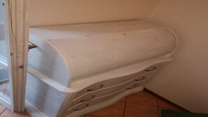 A corner storage unit with multiple drawers and a curved top, placed against a wall in a room with tiled flooring. - Gemini House - Second Floor (Foligno)