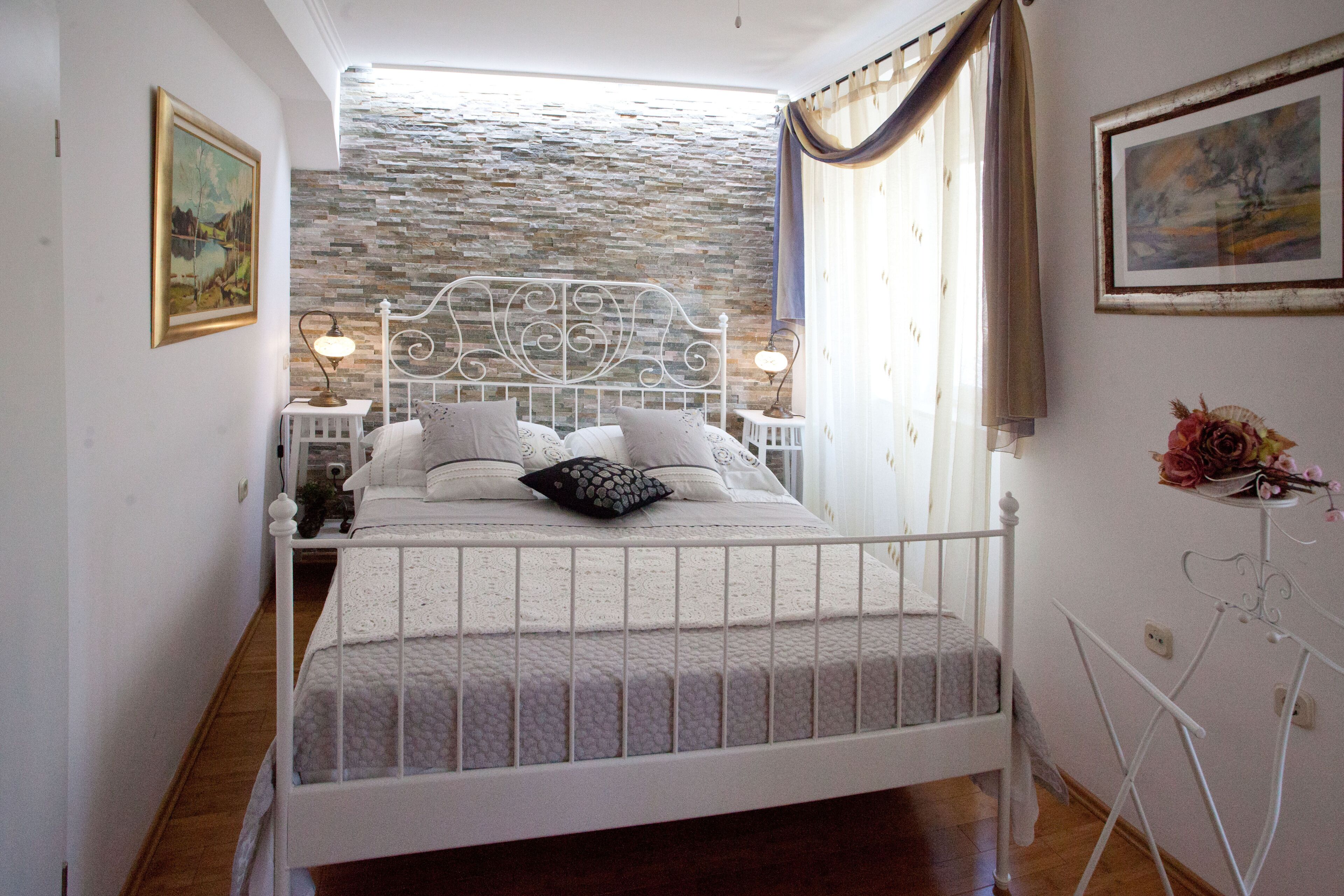 A bedroom with a stone wall, a white bed, two bedside tables with lamps, and a small table with a vase.
