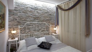A bedroom with a stone wall, a white metal headboard, two bedside lamps, and a bed with multiple pillows. - Split Theatre Apartments (Split)