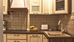 A kitchen with wooden cabinets, a tiled backsplash, a sink, and a fruit basket on the counter. - Split Theatre Apartments (Split)