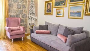 A living room with a stone wall, a pink armchair, a grey sofa, and several framed pictures on the wall. - Split Theatre Apartments (Split)