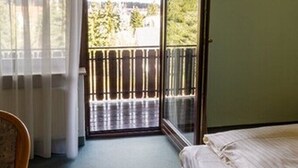 A room with a bed, a chair, a window with curtains, and a sliding glass door leading to an outdoor balcony. - Gasthof Frank (Heroldsbach)