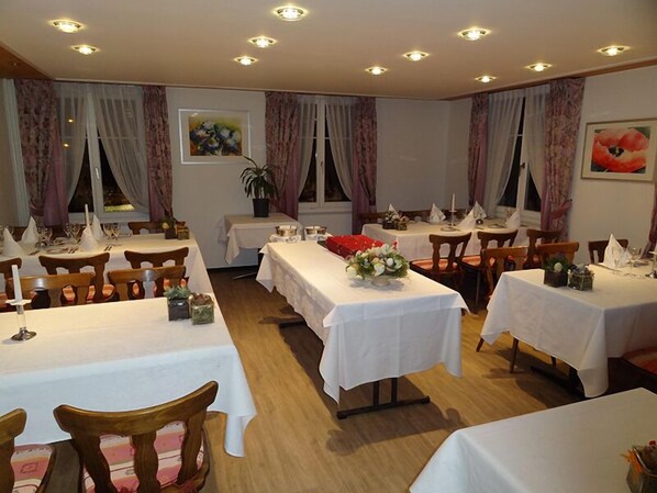Un comedor con varias mesas dispuestas para el servicio, cada una con mantel blanco y distintos cubiertos.
