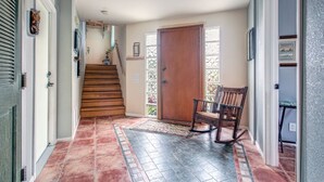 Un pasillo con escaleras de madera, una puerta y un sillón mecedor.