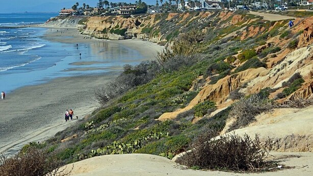 Un paisaje costero con playa, acantilados y una estructura alta.