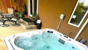 Un jacuzzi con un patio empedrado, mobiliario exterior y un calentador fijado a la pared.