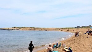 Una playa con gente tomando el sol y caminando por la orilla.