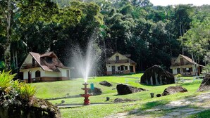 Un jardín con una fuente, dos casas y rocas grandes.