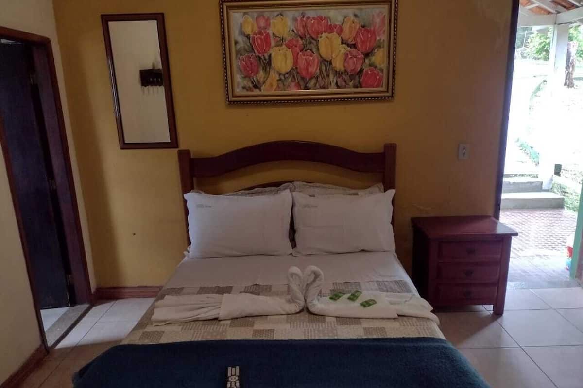 Ein Hotelzimmer mit einem Bett, einem Bild an der Wand, einem Nachttisch aus Holz und einer Tür links.