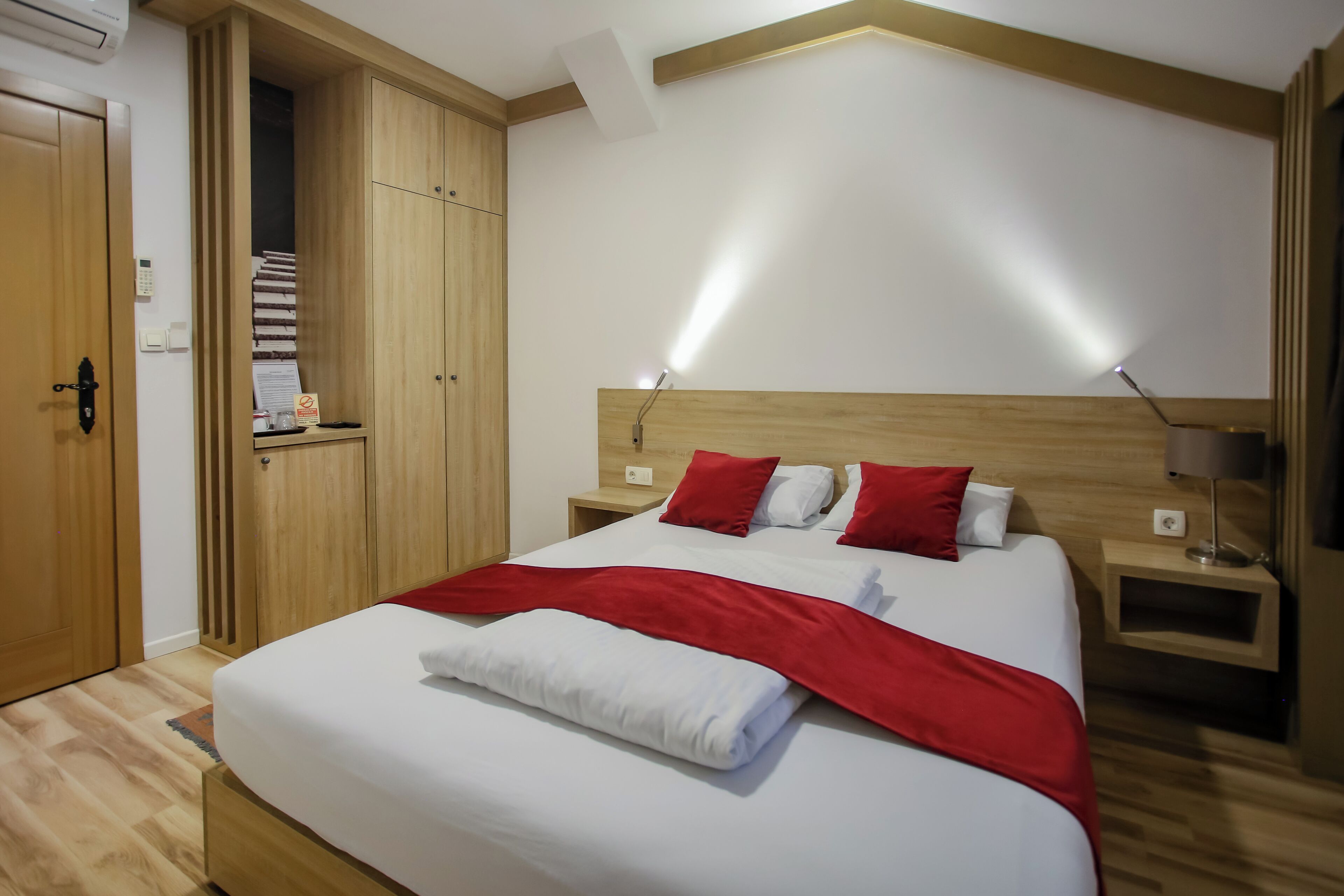 Quarto de hotel com uma cama grande, guarda-roupa de madeira, mesas de cabeceira e um criado-mudo.
