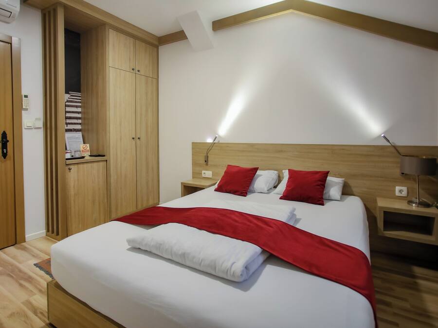 Quarto de hotel com uma cama grande, guarda-roupa de madeira, mesas de cabeceira e um criado-mudo.