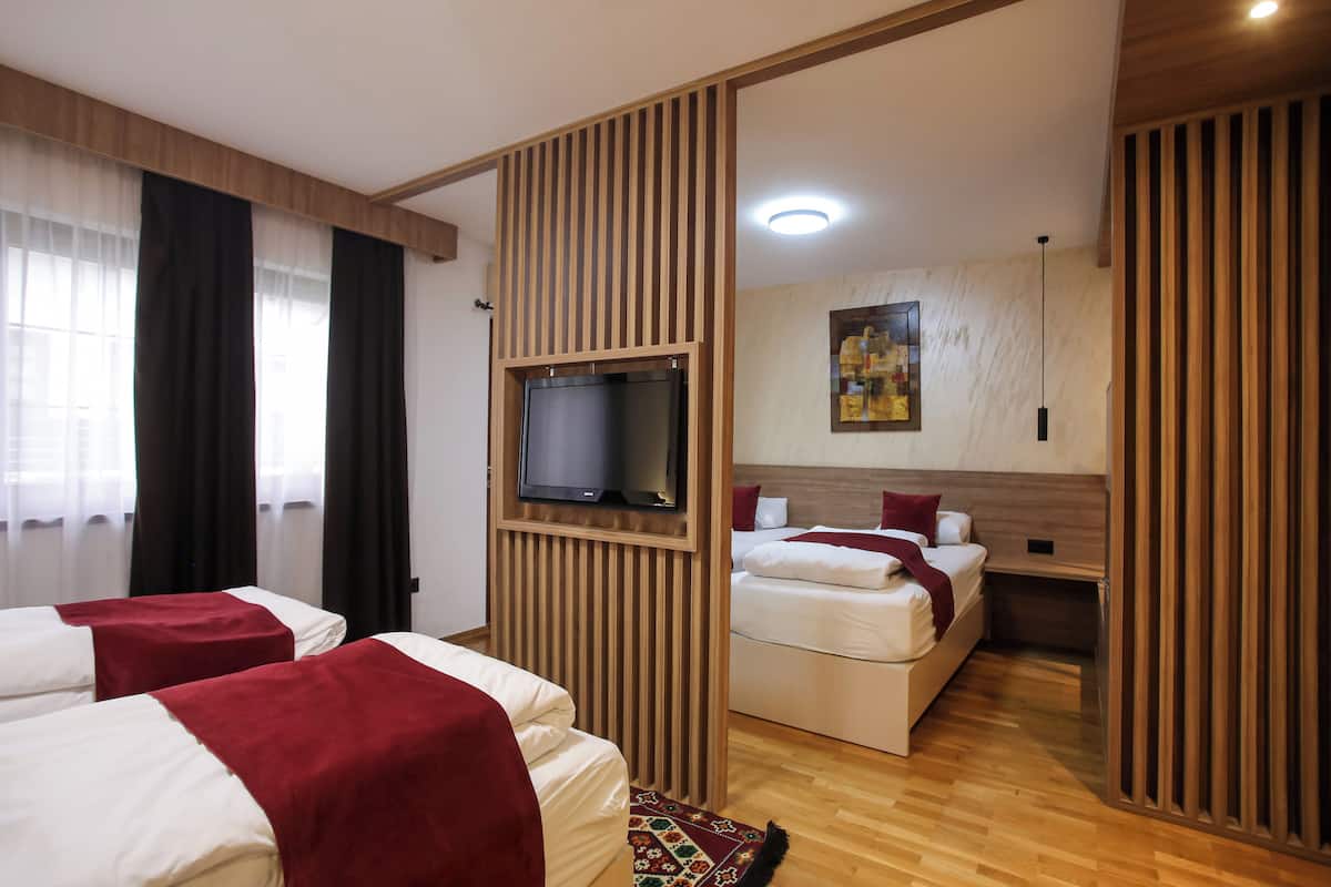 Habitación de hotel con dos camas, un televisor montado en un panel de madera, un cuadro en la pared y suelo de madera.