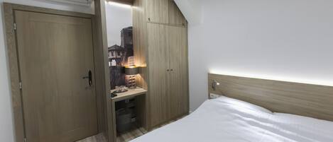 A bedroom with a bed, wooden wardrobe, and a desk with a lamp.