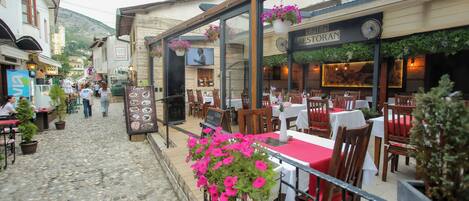 A restaurant with outdoor seating, stone-paved street, and mountain backdrop.