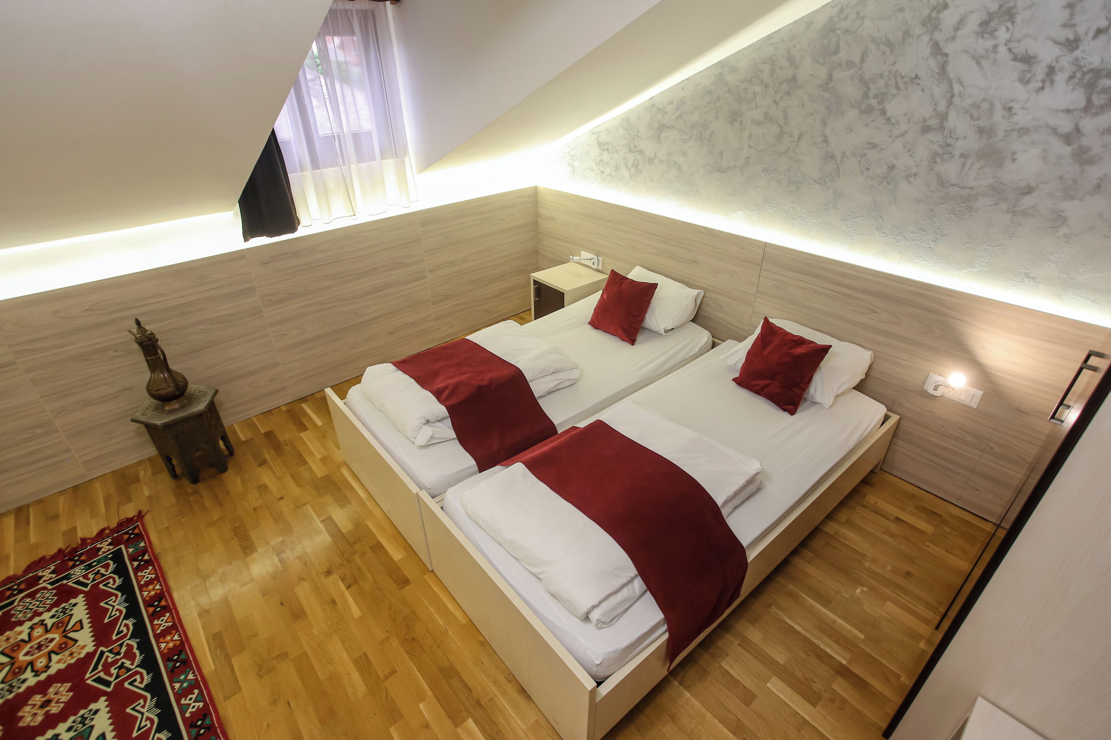 A bedroom with two beds, a nightstand, a decorative vase, and a patterned rug.