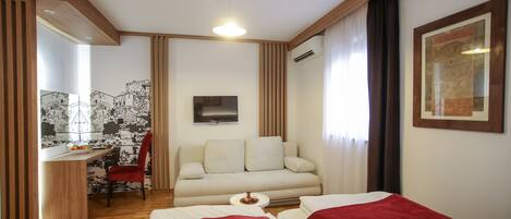 Habitación de hotel con cama, escritorio, silla, sofá y televisor montado en la pared.