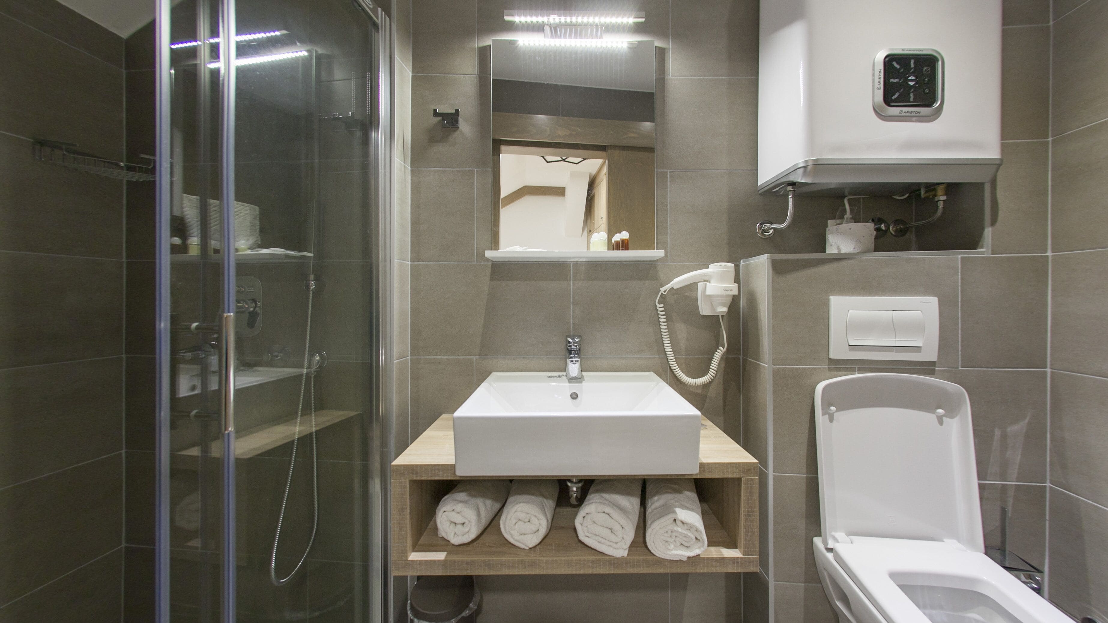 A modern bathroom with a glass-enclosed shower, a sink with a wooden shelf below, and a toilet.