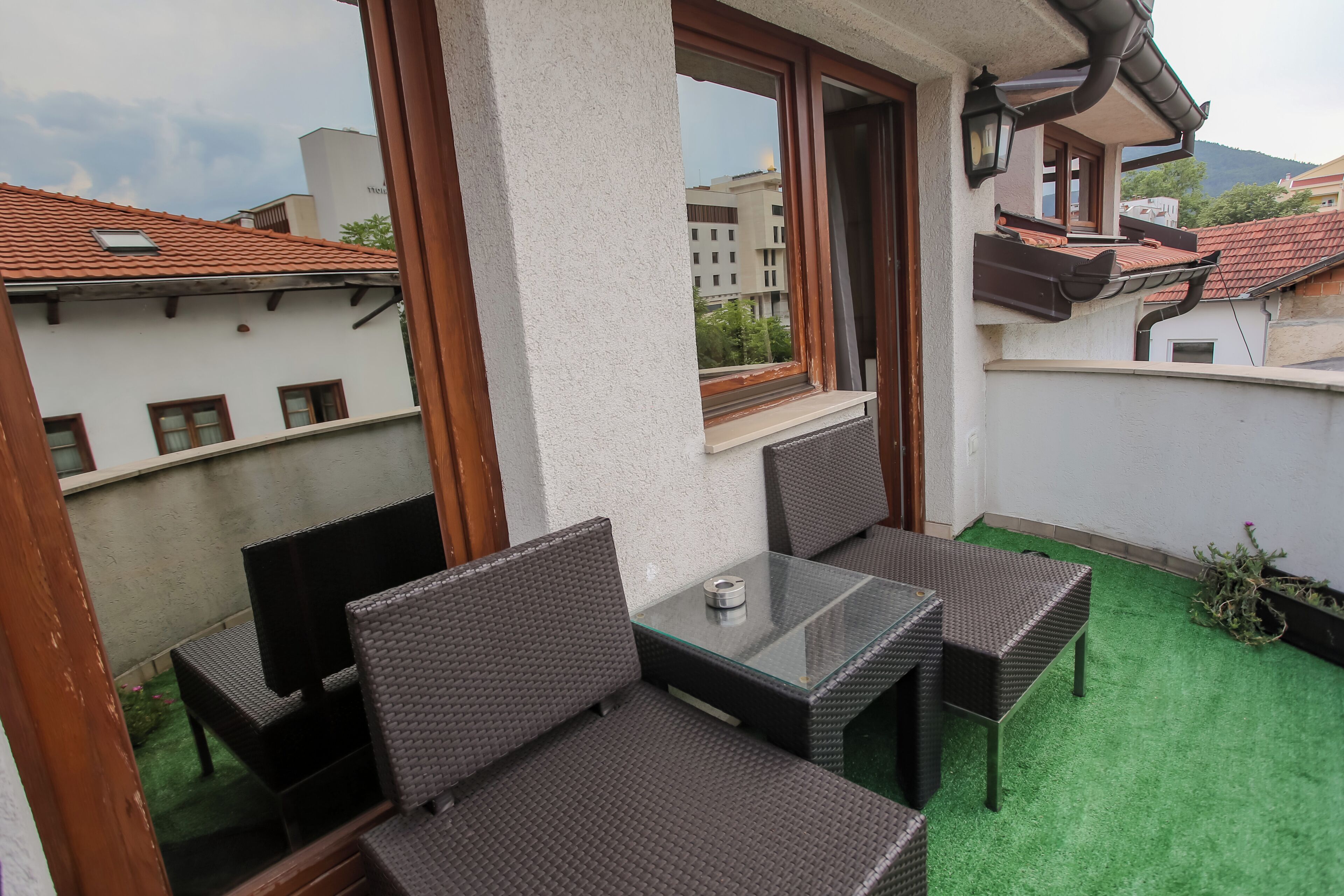 Un balcone con mobili in vimini e un tavolo in vetro, con vista su una città dalle tegole rosse.