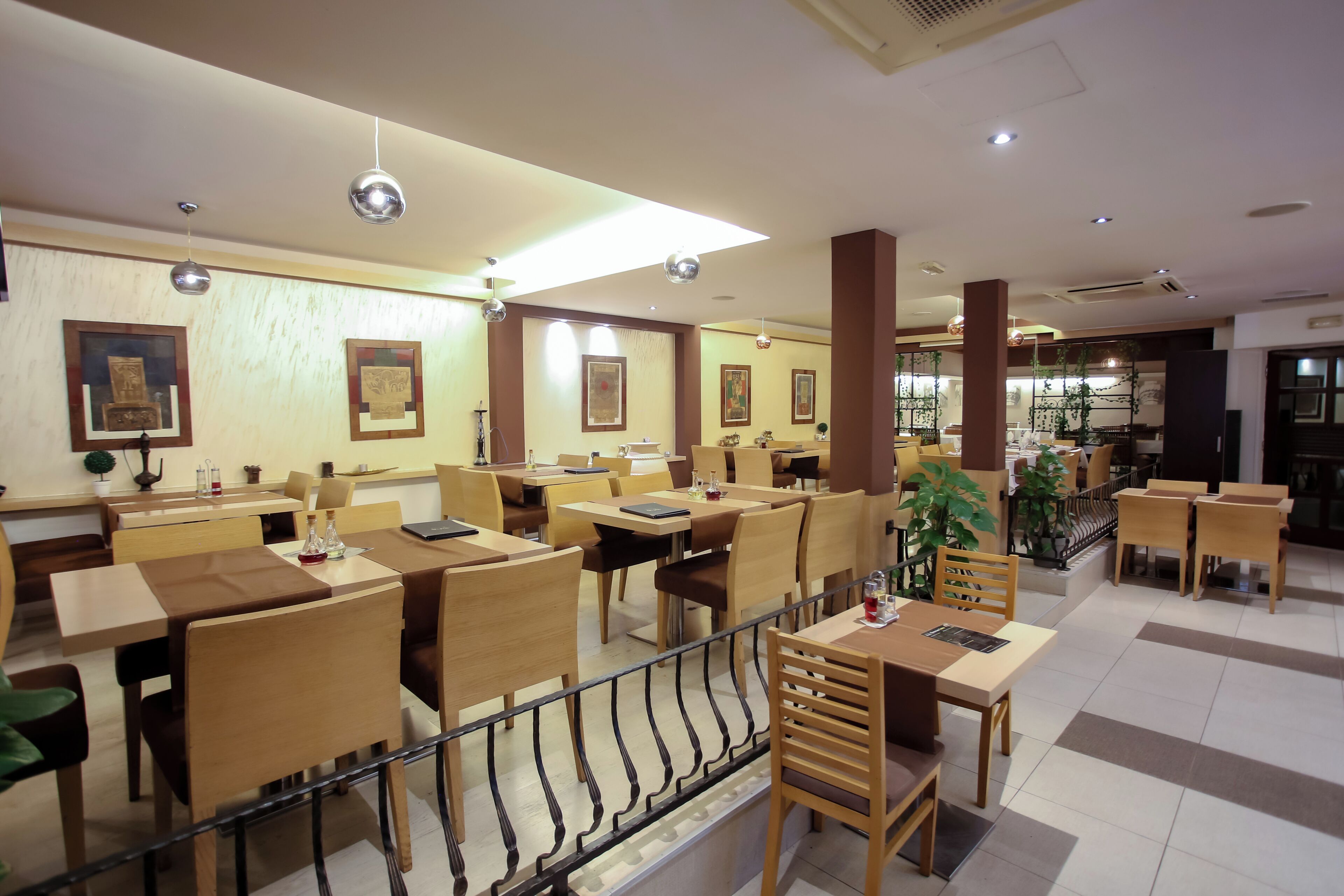 A spacious restaurant with wooden tables and chairs, ceiling lights, and framed artwork on the walls.
