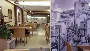 Interior de restaurante com mesas e cadeiras de madeira, plantas penduradas e um mural representando uma cena histórica de uma cidade.