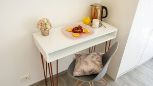 Cozinha moderna com bancada branca, cafeteira, chaleira e um espaço para café da manhã com prato de frutas e sobremesa.