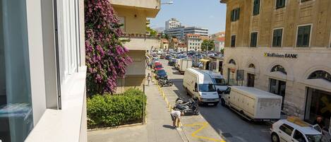 Vista de la calle con vehículos estacionados, un edificio con el rótulo del Banco Raiffeisen y un peatón caminando por la acera.