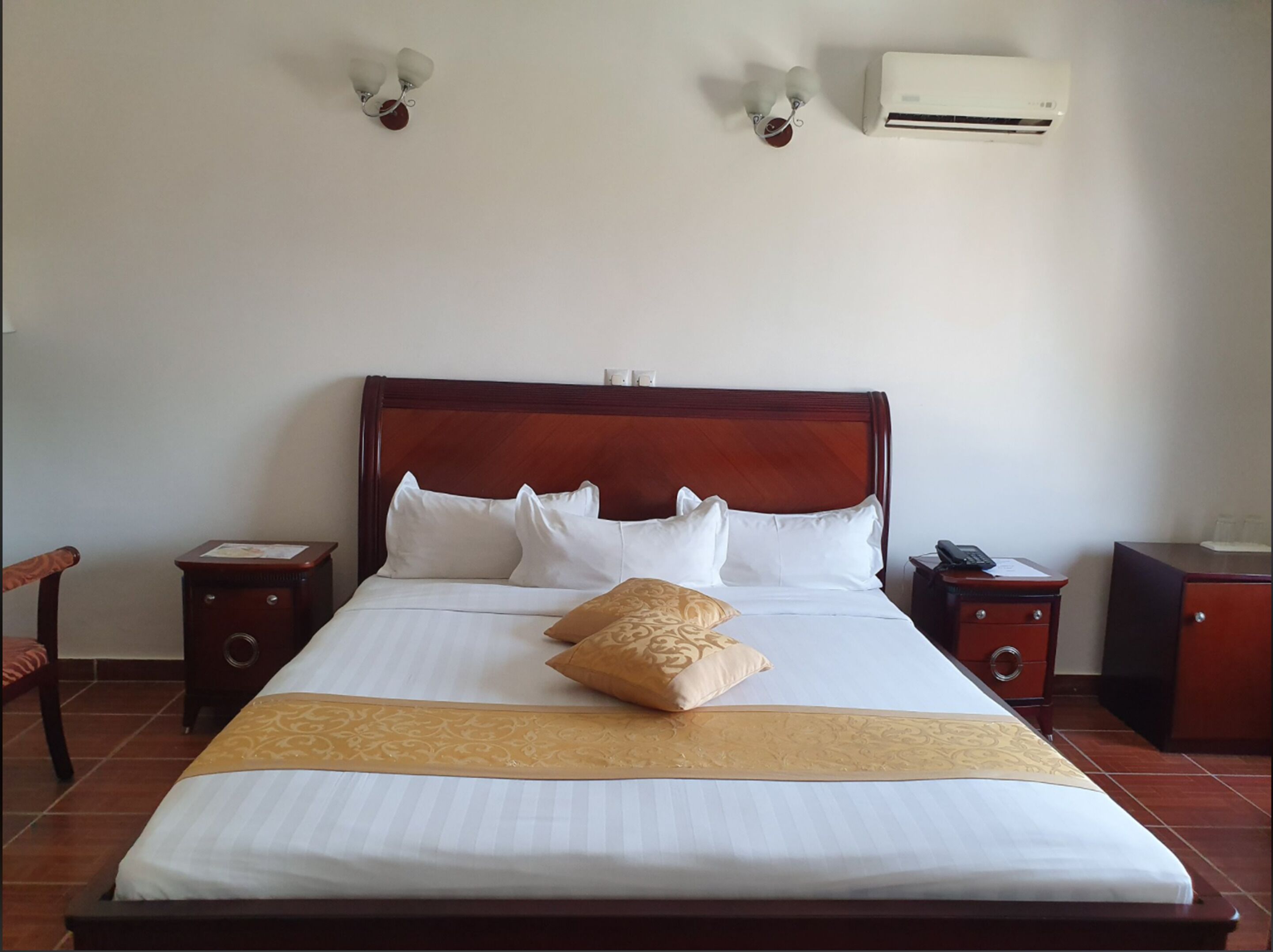Een hotelkamer met een groot bed, twee nachtkastjes, een airconditioning en een wandlamp.