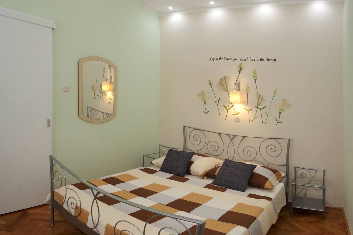 A bedroom with a bed, a mirror, and a wall with a floral light fixture.