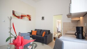 Uma sala de estar moderna com uma mesa de centro de vidro, um sofá preto com almofadas laranja e uma área de jantar com mesa de vidro.