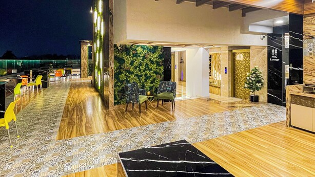 Uma área de estar moderna com piso de madeira, tapetes estampados e uma parede verde com plantas.
