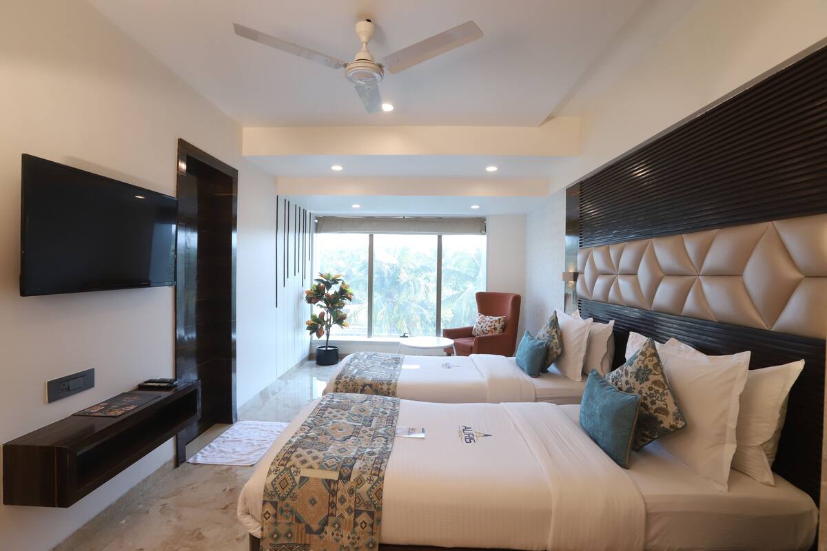 Una habitación de hotel moderna con dos camas, un televisor de pantalla plana, un ventilador de techo y un amplio ventanal con vistas a palmeras.