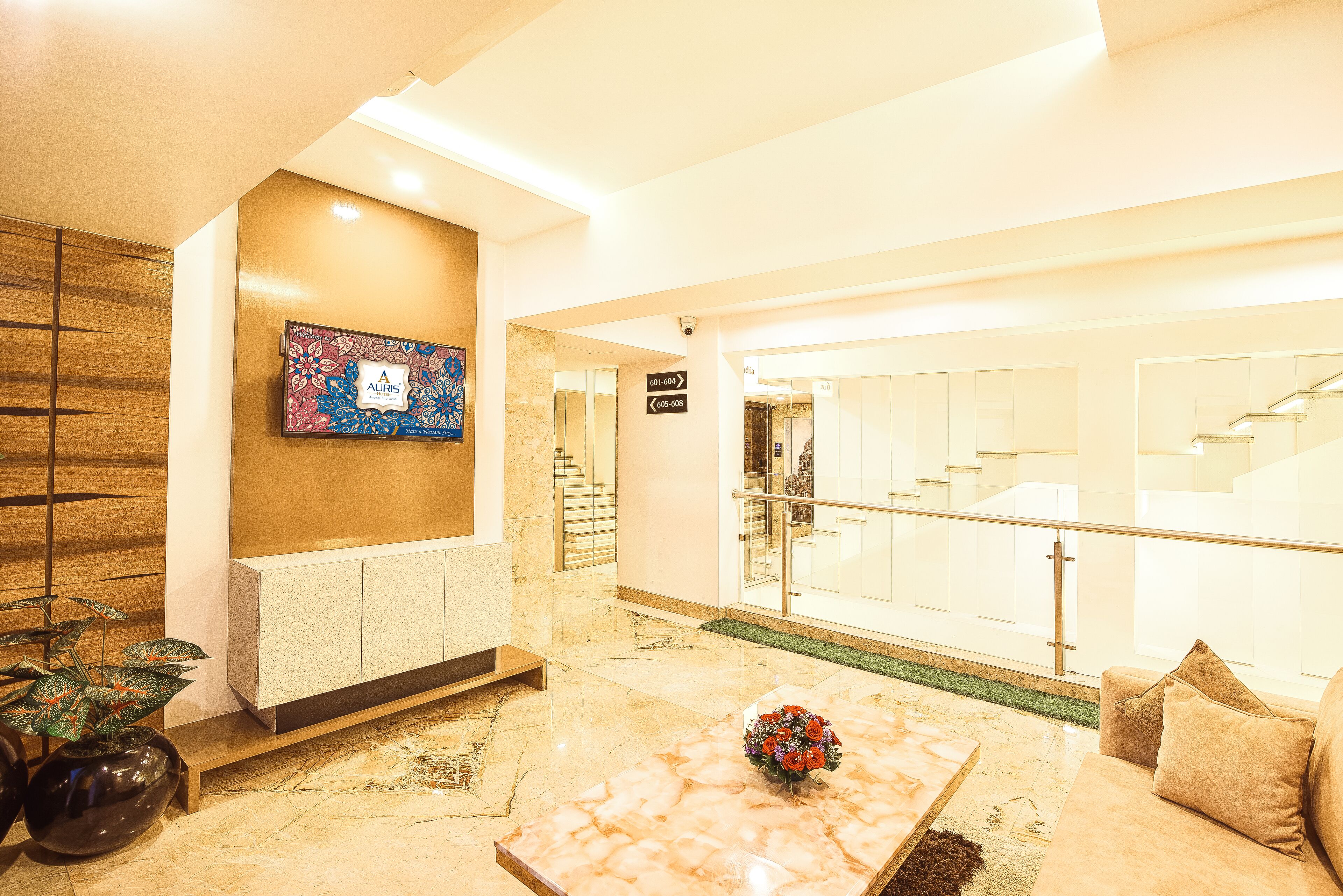A lobby with a marble floor, a reception desk, a television mounted on the wall, and a staircase leading to an upper level.