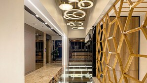 Um hall de hotel moderno com piso de vidro, painel de parede de madeira e luminárias de teto circulares.
