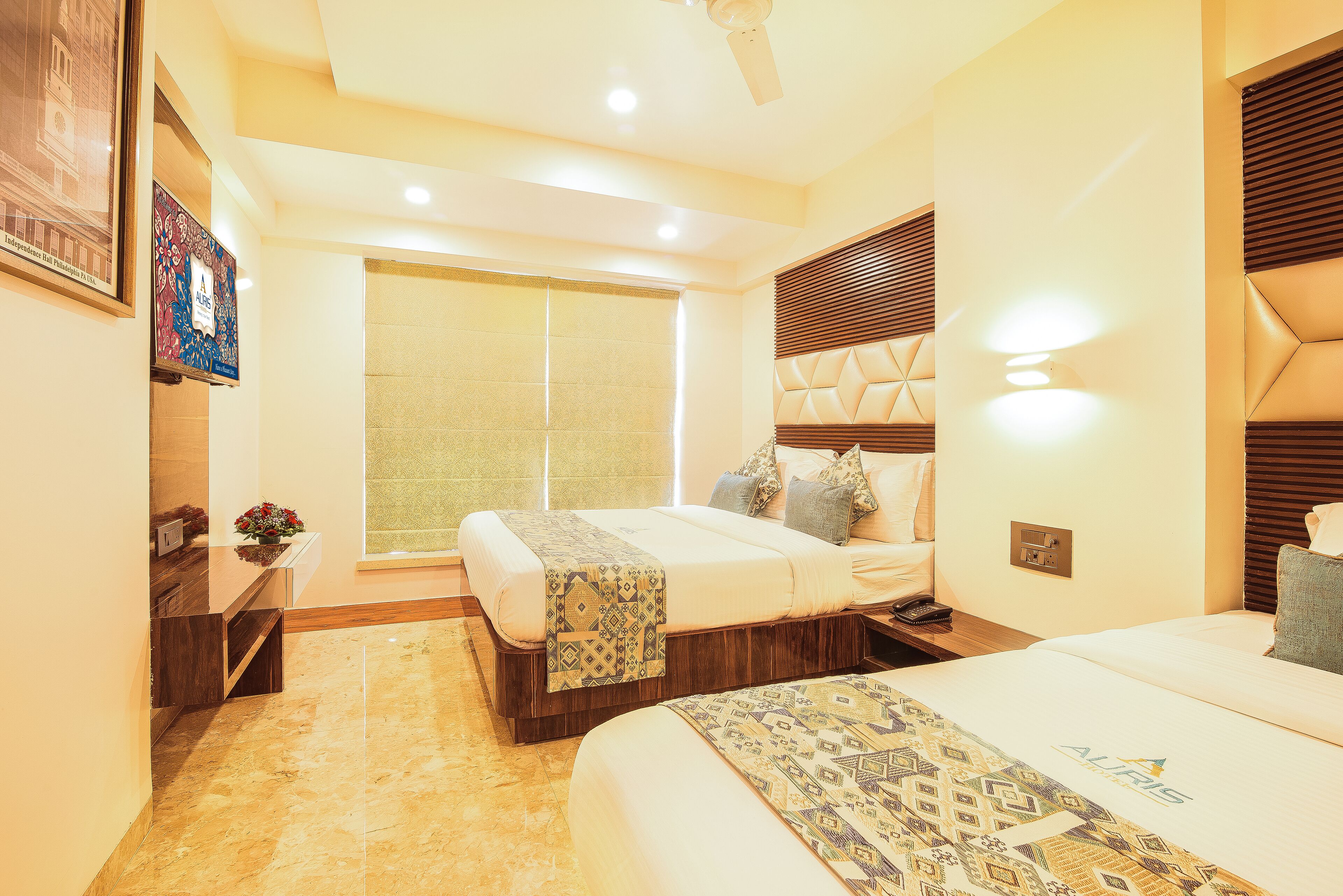 Habitación de hotel con dos camas, un ventanal grande, un ventilador de techo y una lámpara fijada a la pared.
