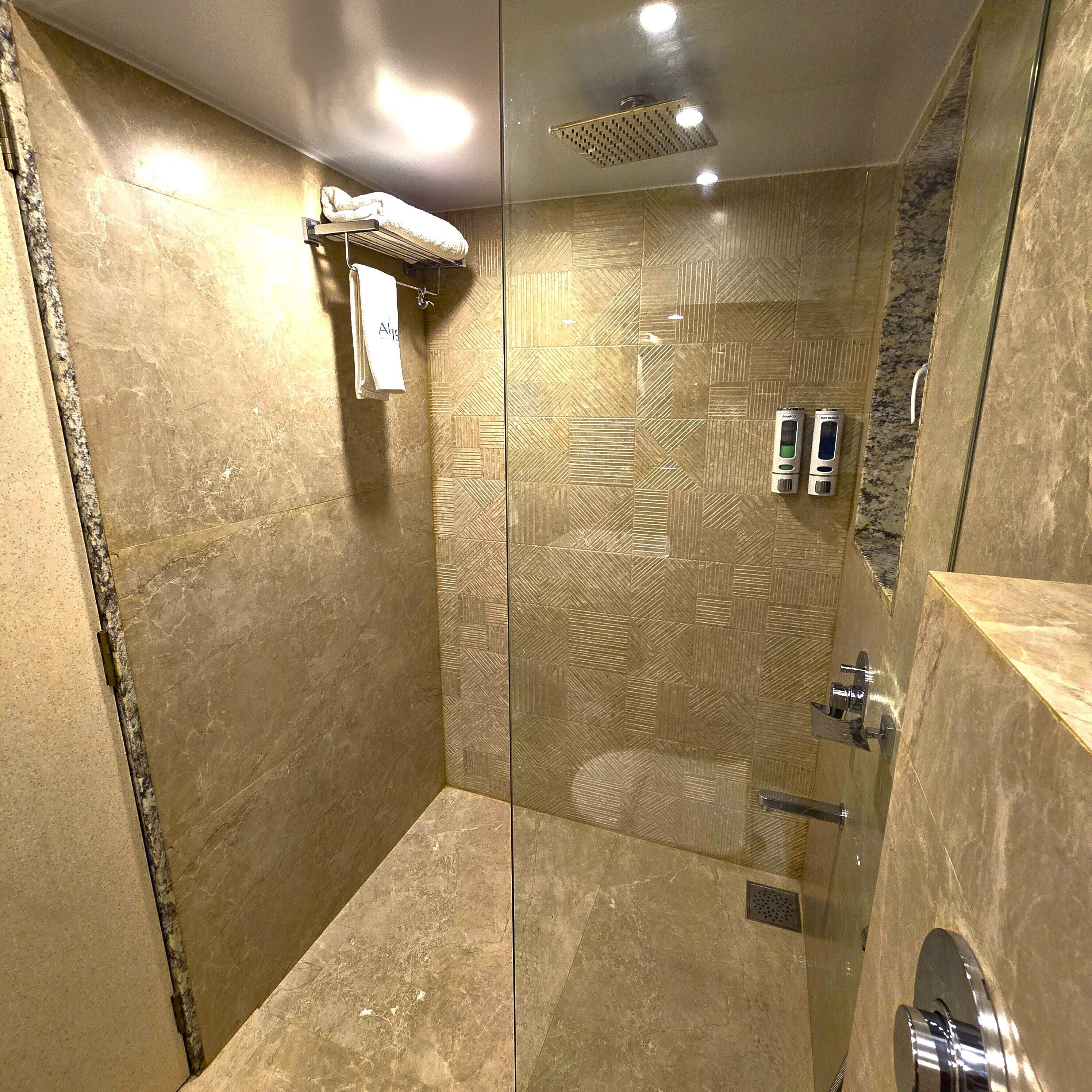 Una ducha con pared de azulejos estampados, un perchero y un cabezal de ducha de mano.