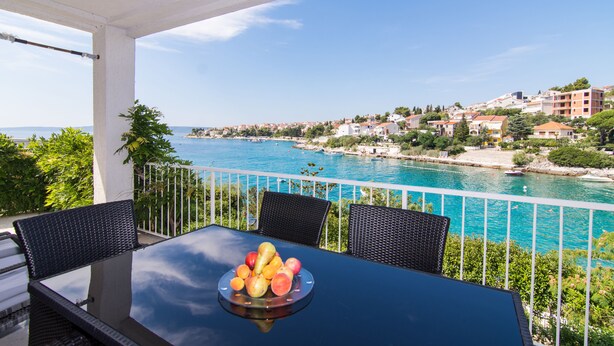A balcony with a table and chairs, overlooking a coastal town with buildings and a body of water. - Cozy Villa in Okrug Gornij with swimming pool and all what is needed (Okrug Gornji)