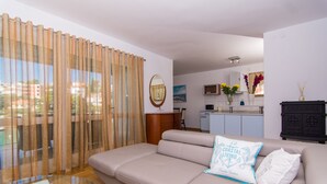 A modern living room with a beige sofa, a glass coffee table, and a view of the city through large windows with beige curtains. - Cozy Villa in Okrug Gornij with swimming pool and all what is needed (Okrug Gornji)