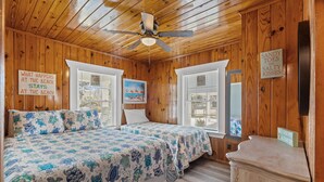 Ein Schlafzimmer in einer Holzhütte mit einem Bett, zwei Fenstern, einem Deckenventilator und einem Schild an der Wand.