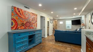 A spacious living room with a blue sofa, a colorful abstract painting, a blue cabinet, and a TV mounted on the wall. - Private Beach House - 1 Block From The Beach + Free Attraction Tickets! (North Myrtle Beach)