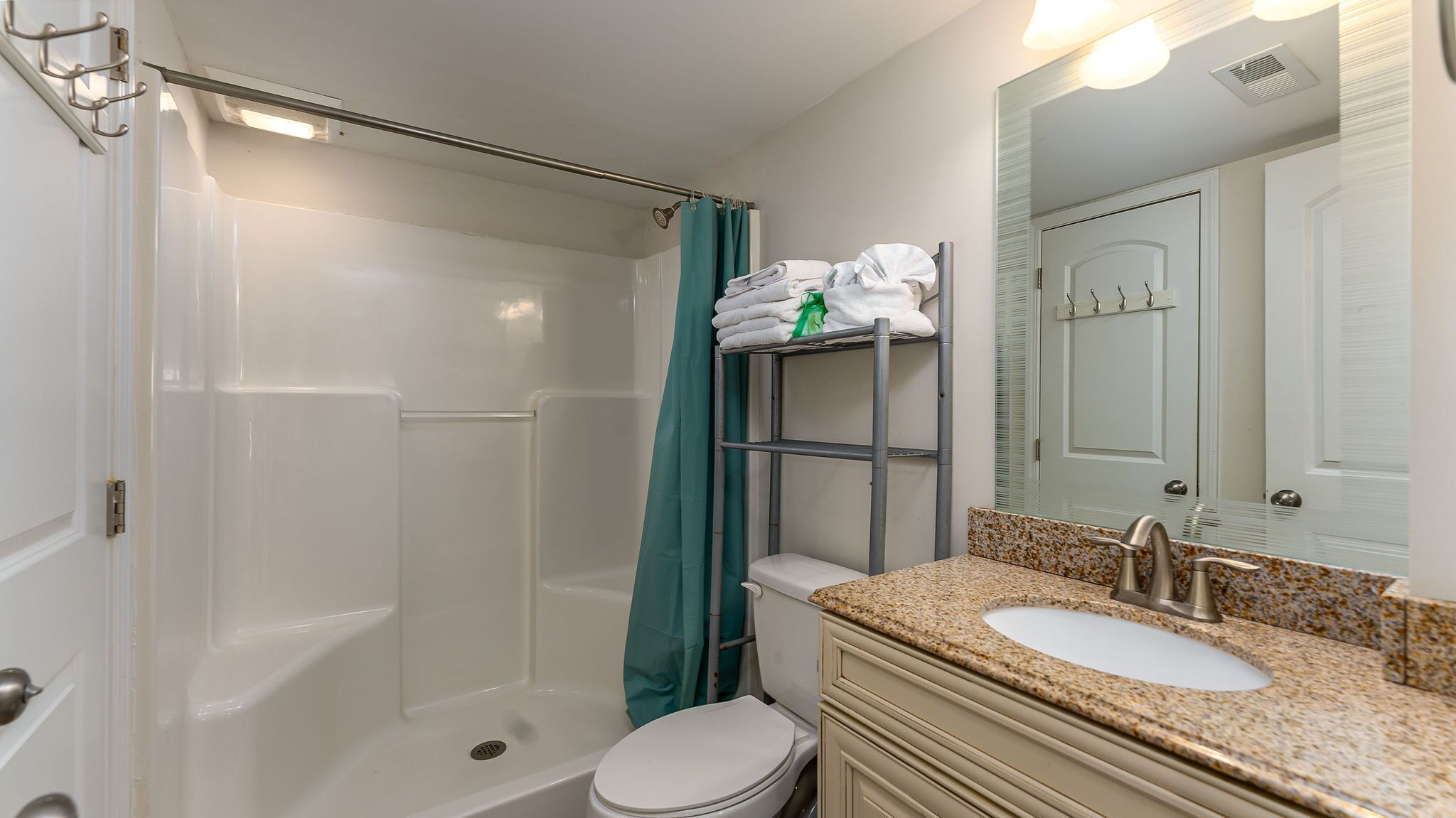 A bathroom with a shower, toilet, sink, and a towel rack with folded towels.