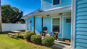 A two-story house with a blue exterior, a front porch with three Adirondack chairs, a small table, and a white picket fence. - Private Beach House - 1 Block From The Beach + Free Attraction Tickets! (North Myrtle Beach)