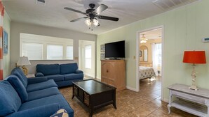 A living room with a blue sofa, a coffee table, a TV on a wooden cabinet, and a ceiling fan. - Private Beach House - 1 Block From The Beach + Free Attraction Tickets! (North Myrtle Beach)
