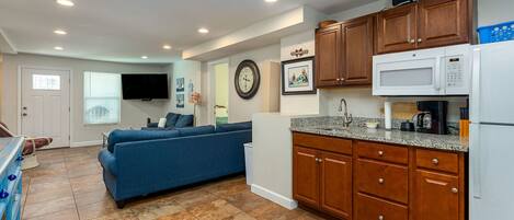 A compact living space with a kitchenette, a blue sofa, a flat-screen TV, and a clock on the wall.