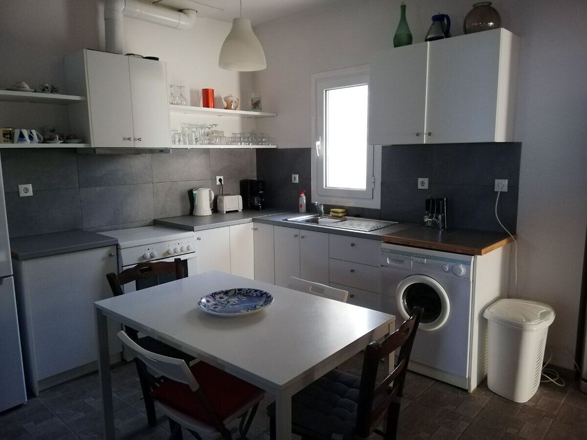 A compact kitchen with a dining table, a washing machine, and a trash bin.