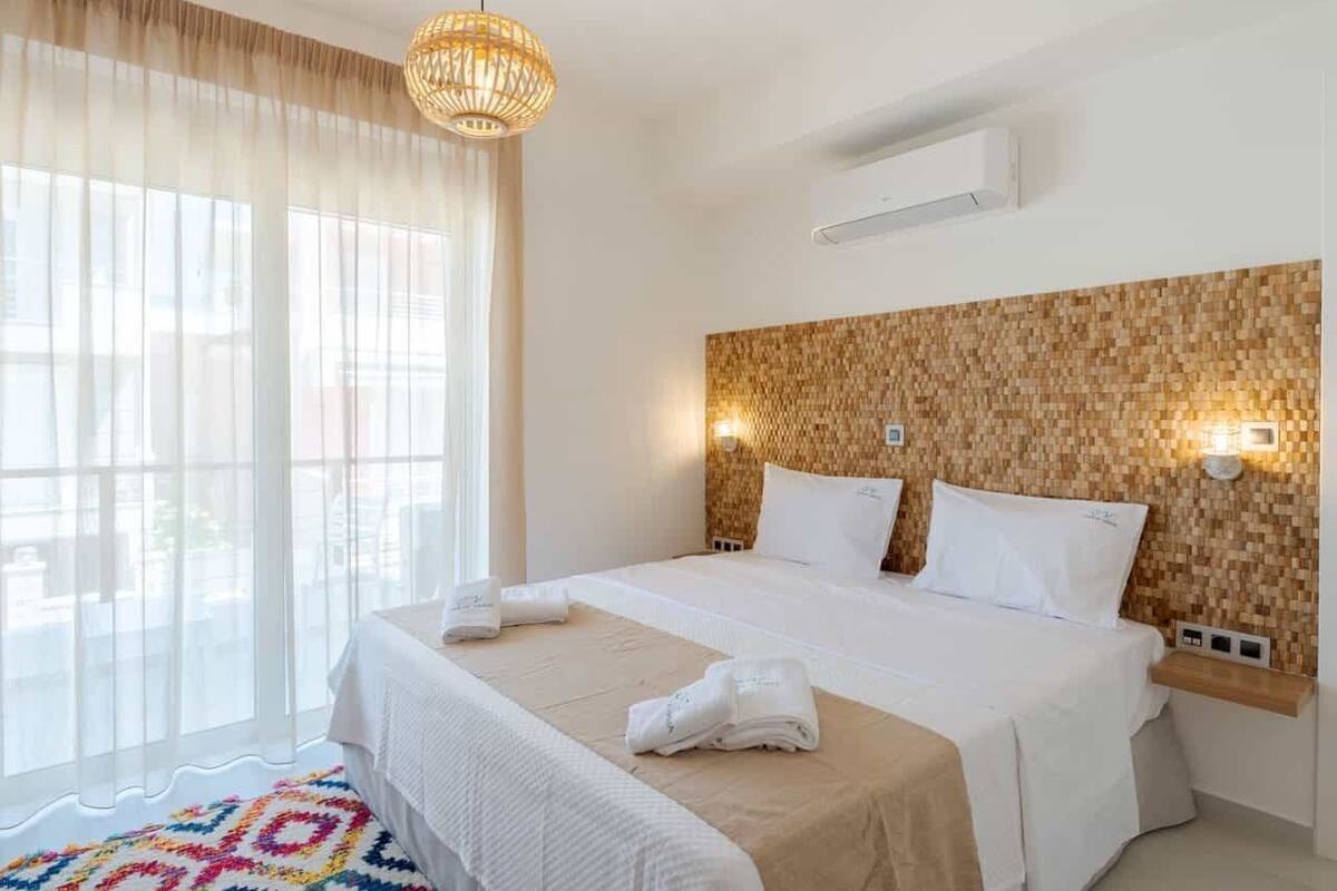 Habitación de hotel con una cama grande, cabecera trenzada y vistas a través de cortinas traslúcidas.